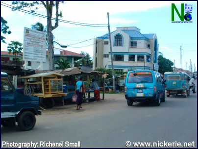 Foto:  Guyanezen nabij de grens met Suriname, opgeschrikt door een brute bankoverval op klaarlicht dag te Rosehall. De foto is gemaakt vanuit de Openbare markt van Skeldon in Guyana, op de achtergrond een van banken, die vanwege het voorval gesloten bleef voor het publiek. 