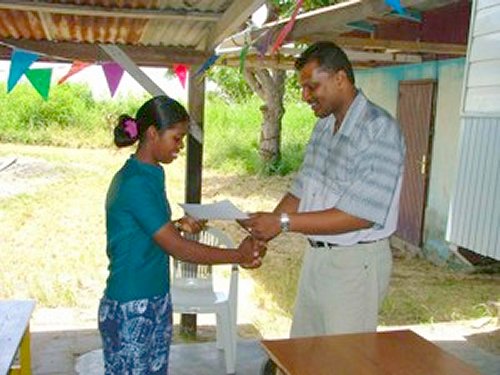  filiaalhouder van de RBTT bank de heer Adhin overhandigt aan de cursist Sharda Ghra haar certificaat.